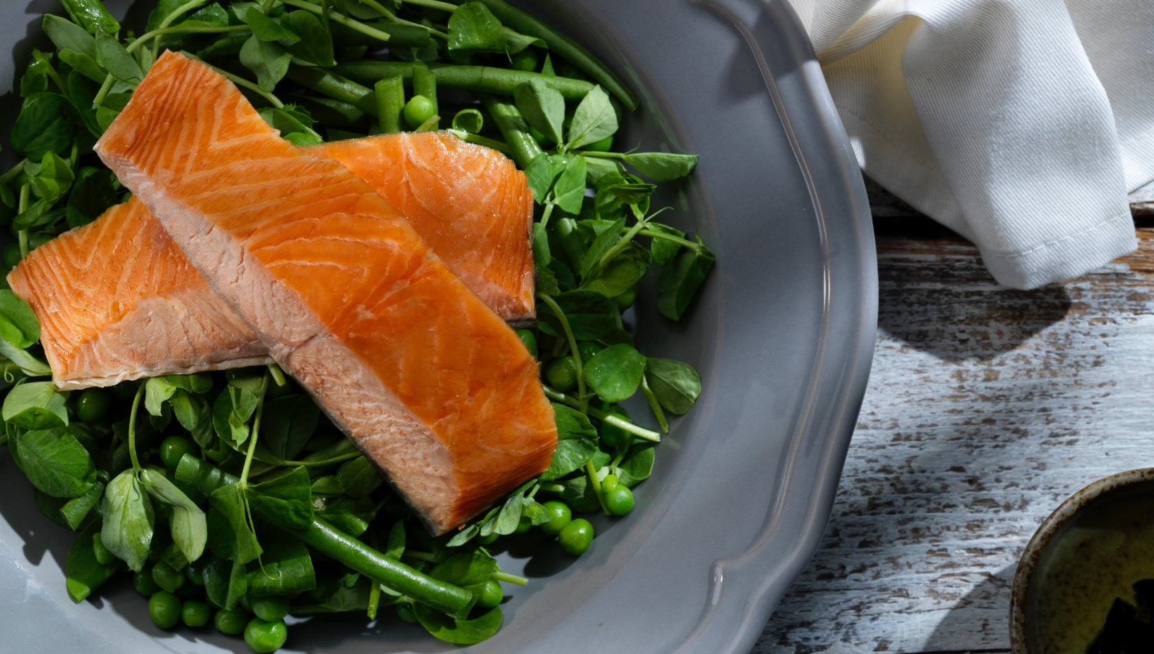 Two fillets of salmon resting on a bed of greens, beautifully presented on a grey plate.