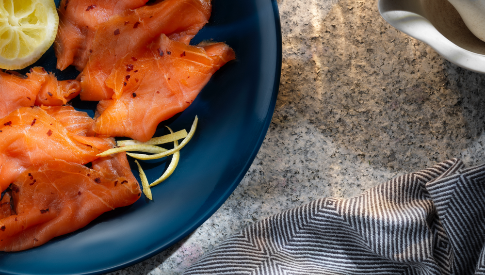 Smoked salmon with flakes of chilli and the rind of a fresh lemon, all resting on a blue dinner plate.
